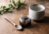 Tmavá živica shilajit v sklenenej nádobke vedľa drevenej lyžice a šálky teplej vody