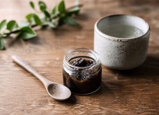 Shilajit pod lupou: čo dokáže himalájska živica a ako ju užívať Tmavá živica shilajit v sklenenej nádobke vedľa drevenej lyžice a šálky teplej vody